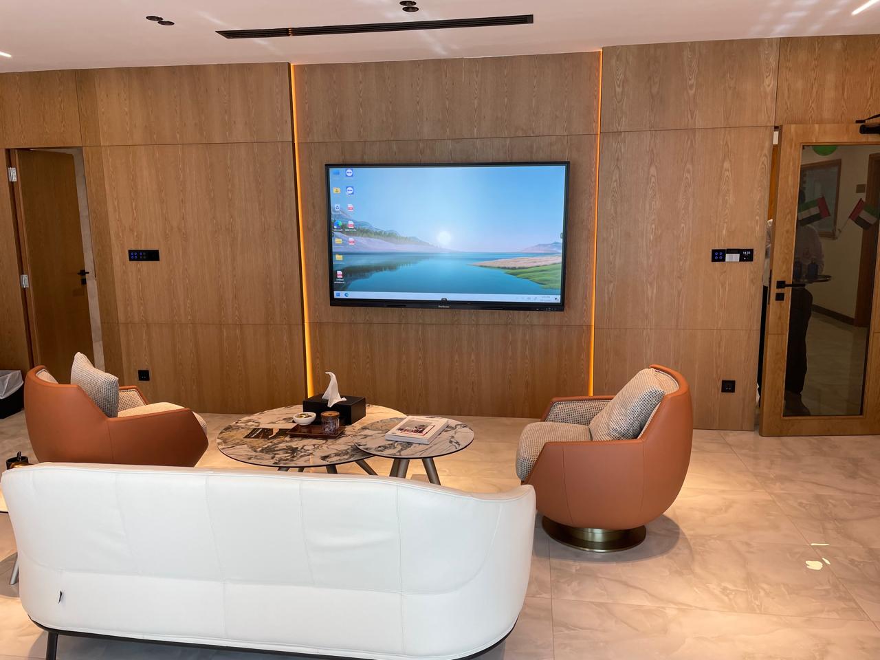 Modern living room with white sofa, brown armchairs, and a large TV on the wall.